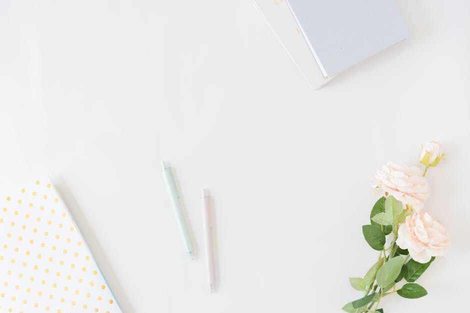 A clean and simple flat lay of notebooks, pens, and flowers on a white background.
