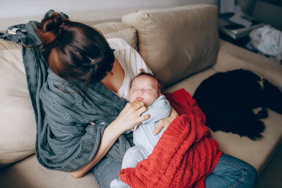 A tender moment of a mother comforting her sleeping baby while resting on a sofa indoors.