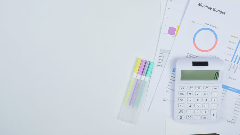Minimalist office desk with a calculator, budget planning documents, and colorful pens.