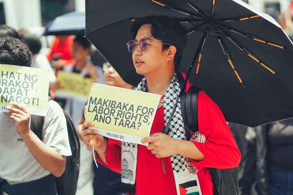 Protest for labor rights featuring diverse participants holding placards and an umbrella for shade.
