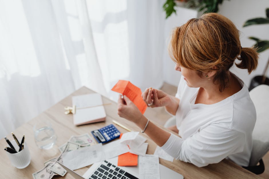 A woman organizing her finances with bills and receipts at a home office desk using a calculator and laptop.