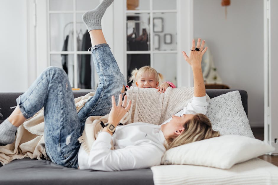 A joyful mother and her young daughter playfully relax on a couch in a cozy room.