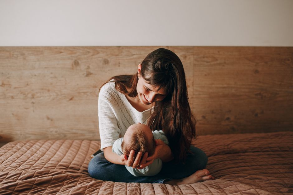 A heartwarming scene of a mother gently holding her baby on a bed, captured in a cozy bedroom setting.