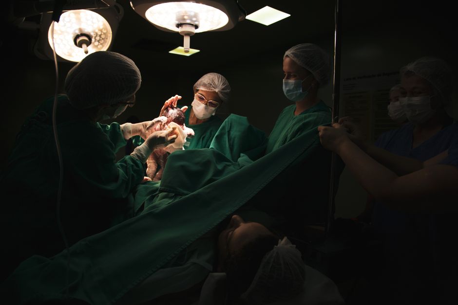 Doctors and nurses delivering a newborn baby under surgical lights in a hospital.