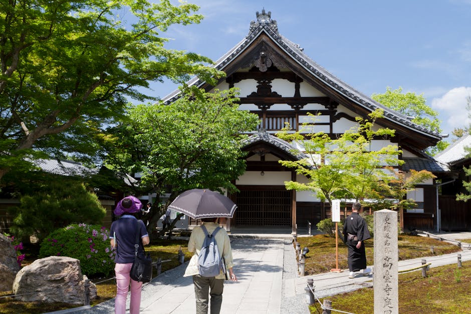 Visitors at a traditional temple in Kyoto, Japan surrounded by lush greenery and historic architecture.