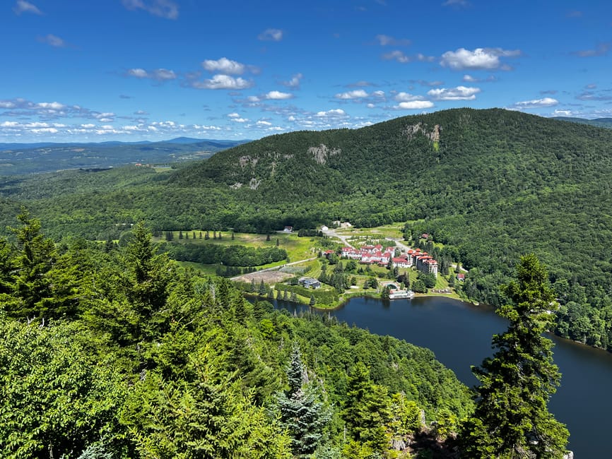 A breathtaking aerial view of lush green mountains and a serene lake under a clear blue sky.