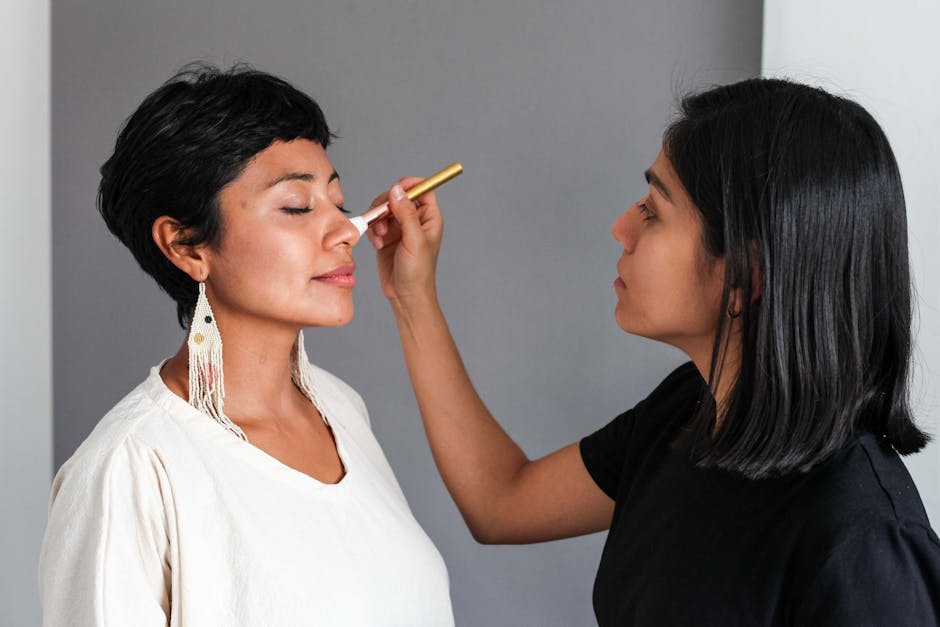 A makeup artist expertly applies cosmetics to a woman indoors.