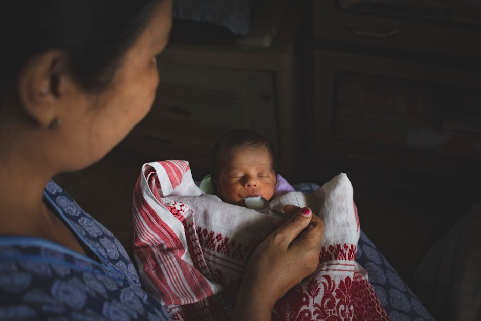 A heartwarming scene of a mother gently feeding her newborn with a spoon, wrapped in a cozy blanket.