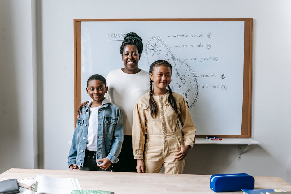 Smiling black woman embracing diverse schoolchildren while standing against whiteboard in school and looking at camera