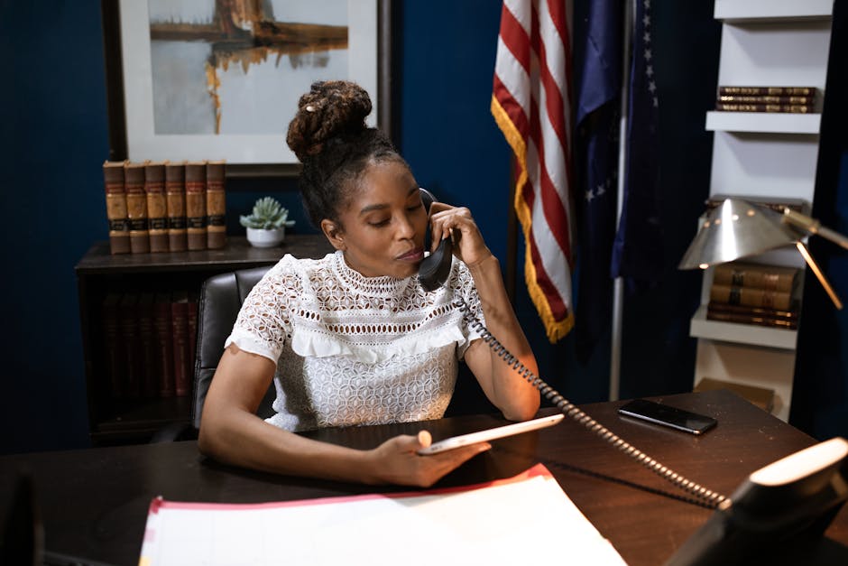 Businesswoman multitasking with phone and tablet at desk in office setting.