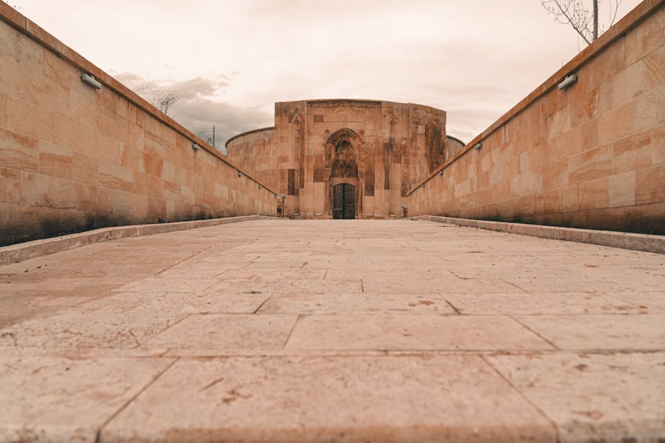 A historic sandstone building with a gated entrance, surrounded by walls under a cloudy sky.