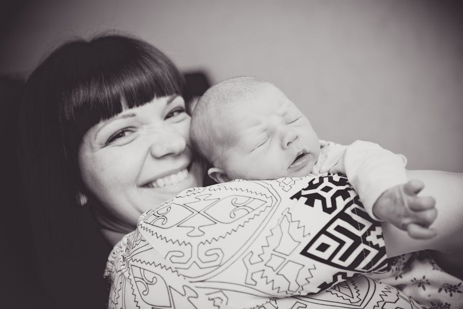Black and white portrait of a smiling mother holding her sleeping newborn lovingly.