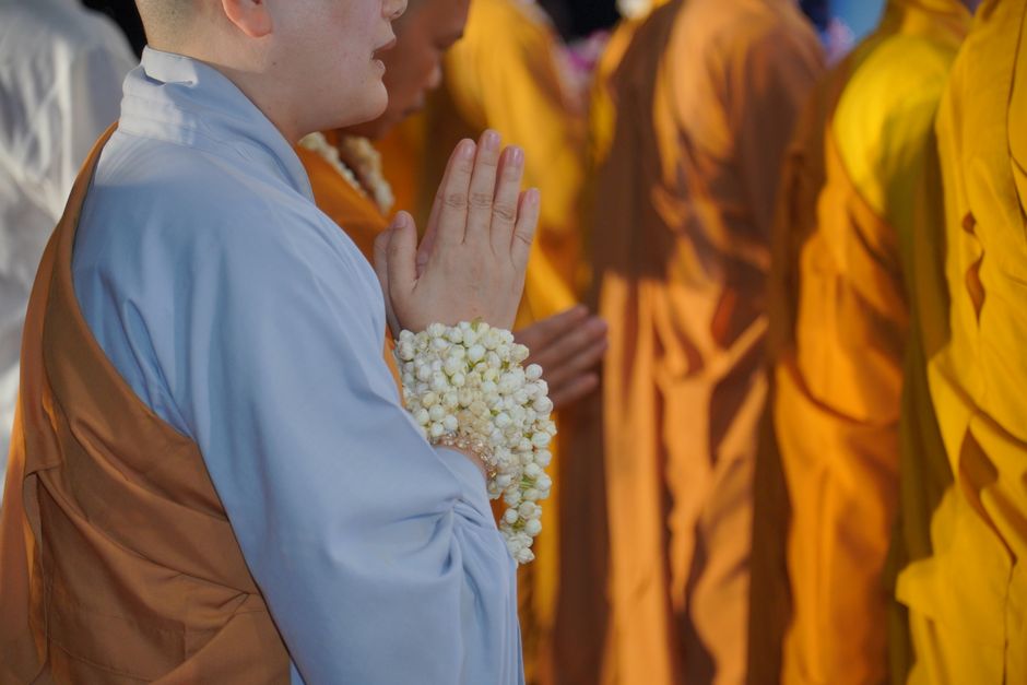 A group of monks dressed in traditional robes participate in a solemn outdoor prayer ceremony.