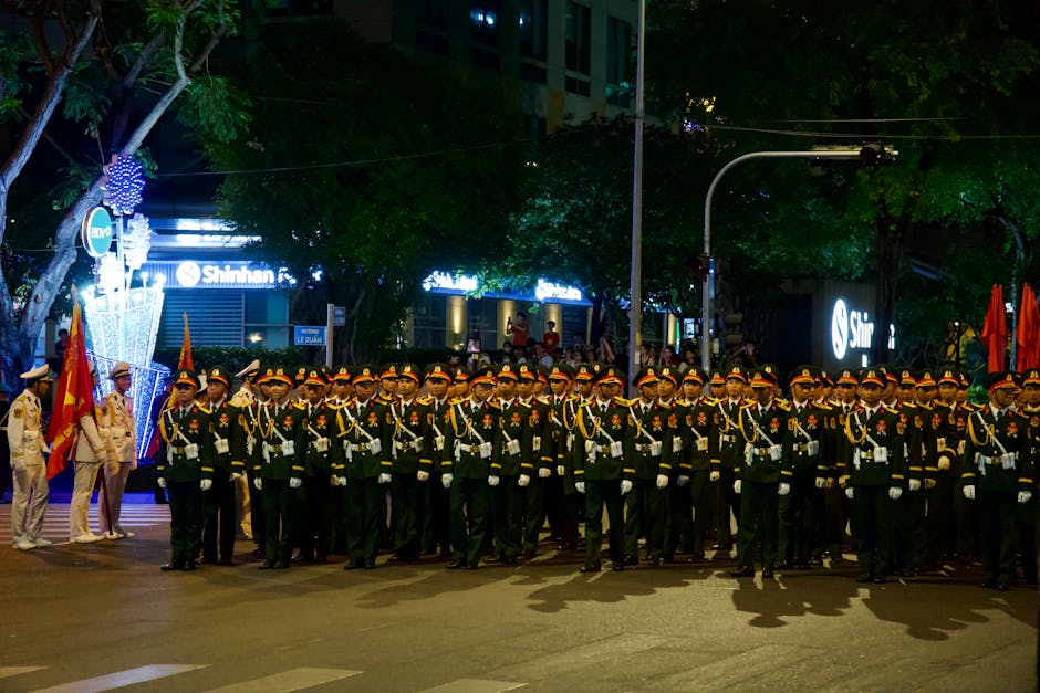 A group of uniformed soldiers stand in formation during a nighttime parade on a city street.