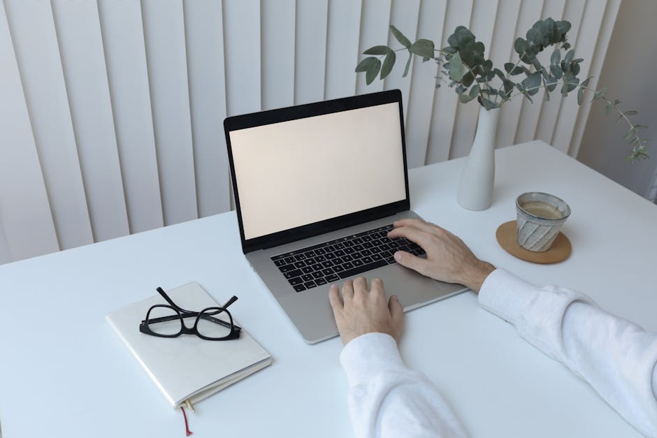 High angle of crop faceless person sitting at table with cup of hot coffee and notepad while working on netbook
