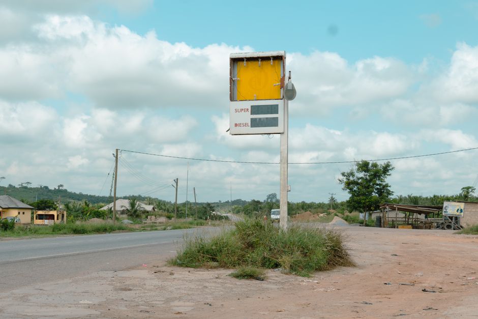 Deserted roadside gas station sign on a rural highway with cloudy sky.