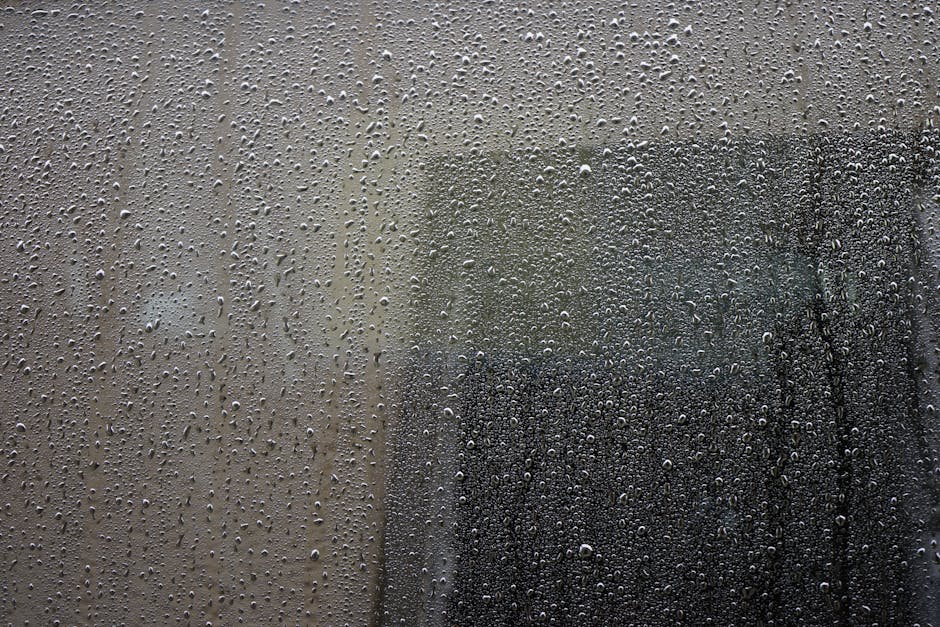 Close-up of a rain-drenched window covered in water droplets, showcasing abstract urban atmosphere.