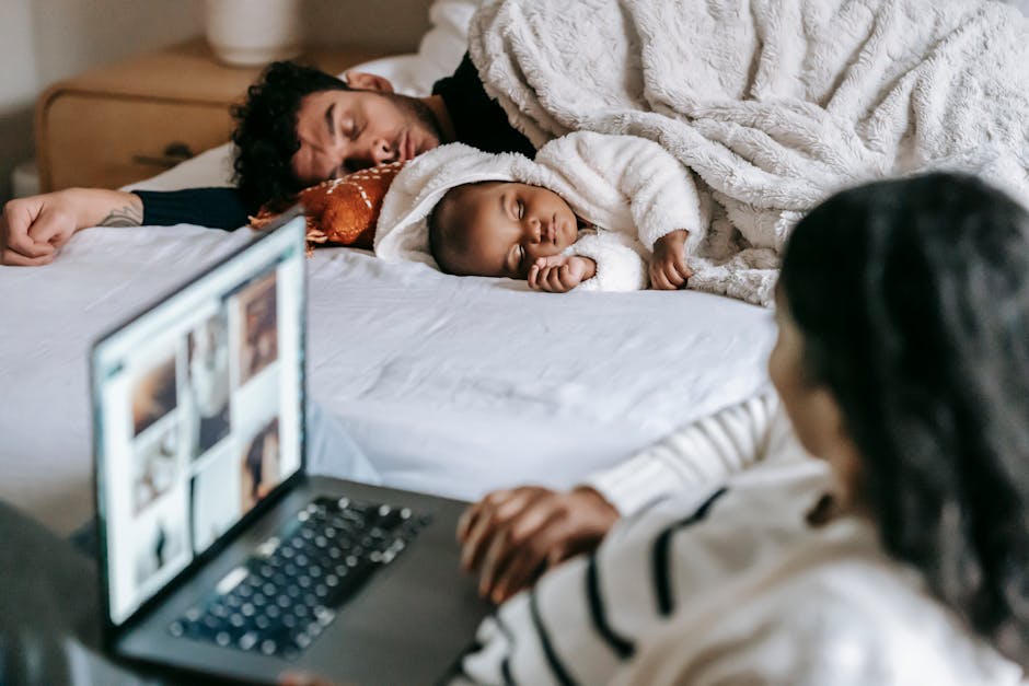 High angle of cute multiracial baby with father sleeping on comfy be near unrecognizable mother working remotely on laptop