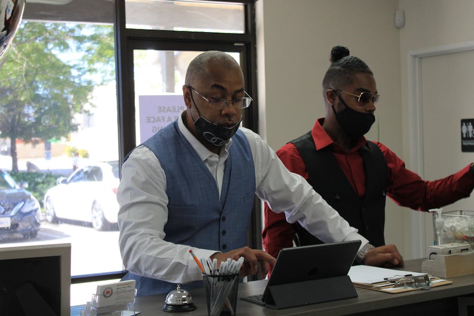 Two men in masks working and collaborating with a tablet in a modern office setting.