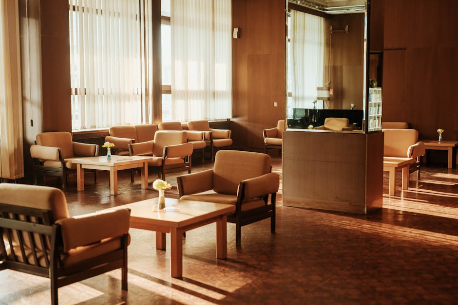A cozy and retro-style lounge area with warm sunlight, armchairs, tables, and windows.