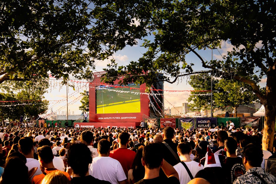 Crowd gathered in İstanbul park watching Euro football on big screen. Energetic summer atmosphere.