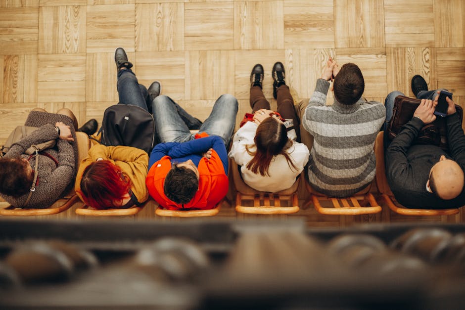 Top view of adults sitting in a row on wooden chairs on a parquet floor indoors.