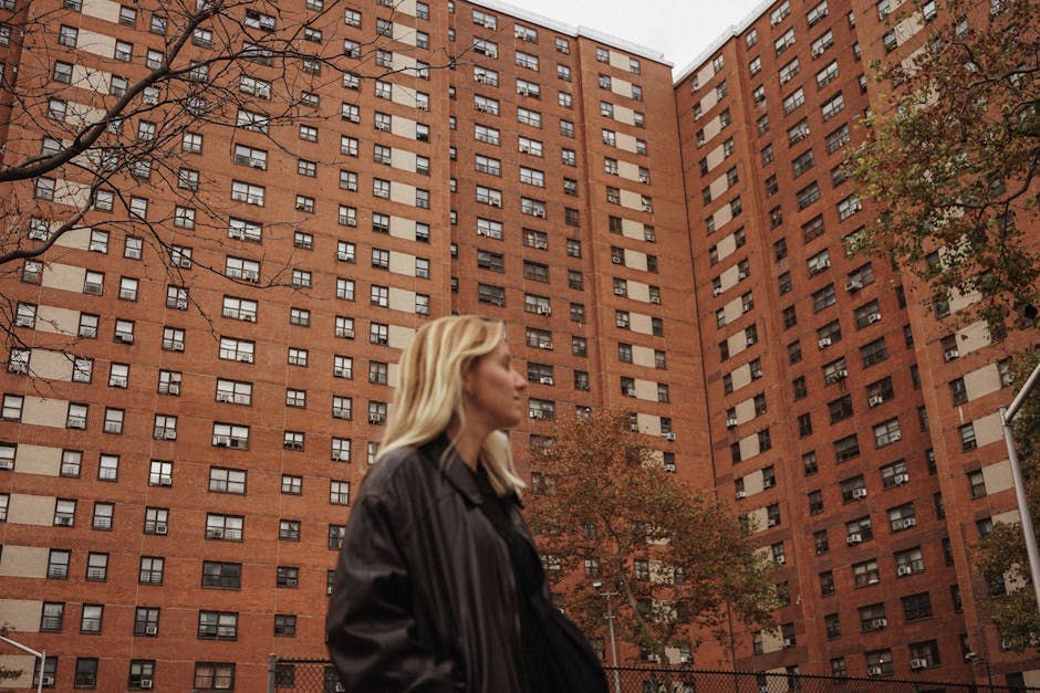 A woman walks by towering urban buildings with a moody urban backdrop.