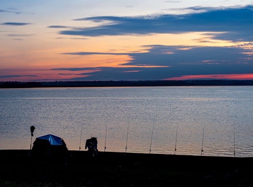 Tranquil lakeside view at sunset with a tent and fishing rods on the shore.