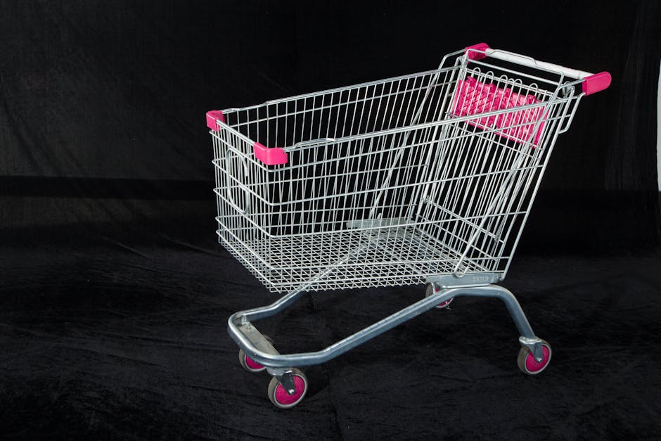 A metal shopping cart with pink handles and wheels on a dark backdrop, ideal for retail and commerce themes.