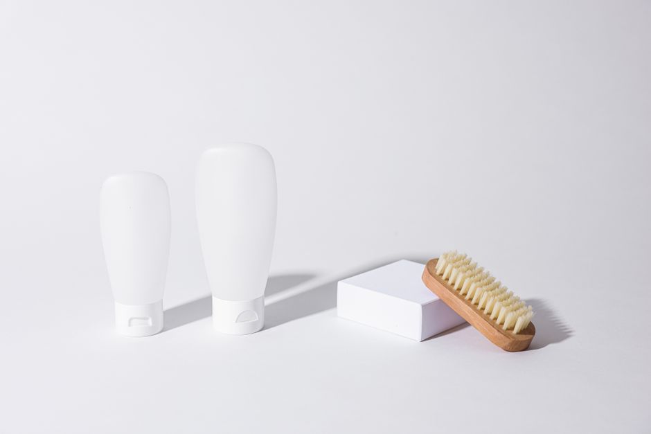Clean minimalist photo of skincare bottles with a wooden brush on a white background.