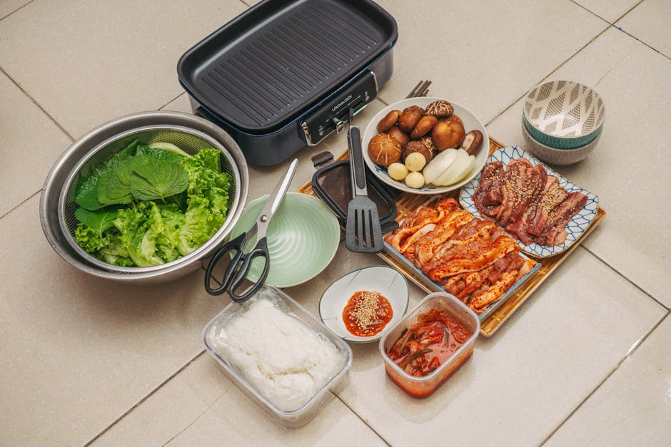 A complete Korean BBQ setup with meat, vegetables, kimchi, sauces, and grill ready for cooking.