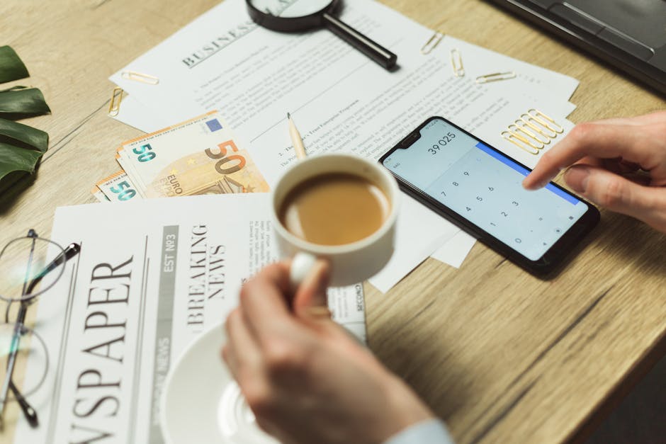 High-angle view of a business workspace with documents, coffee, currency, and smartphone calculator.