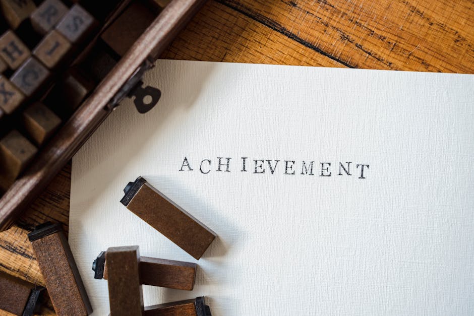 A close-up of wooden stamp typography creating the word 'achievement' on white paper.