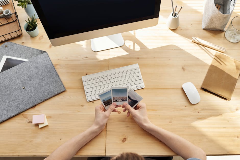 A cozy home office desk setup with hands holding printed photos, capturing a moment of nostalgia and creative inspiration.