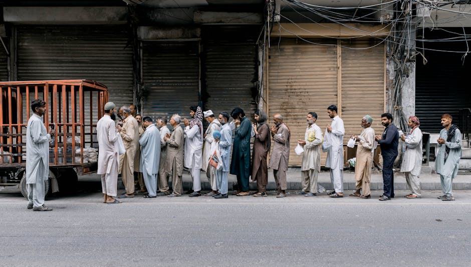 A group of adults standing in line for charity aid on a city street in Faisalabad, Pakistan.