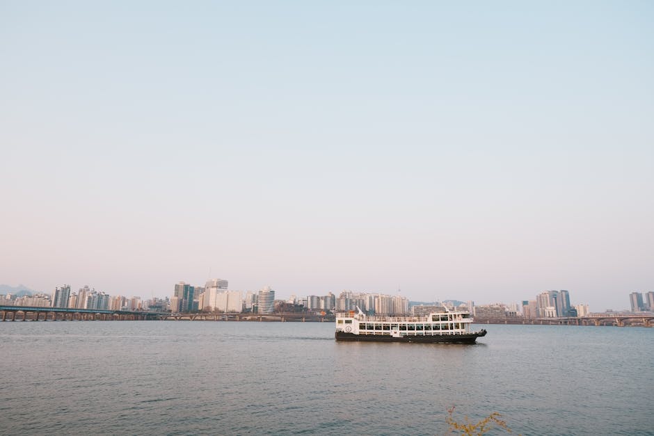 A scenic view of a city skyline with a ferry navigating the river under a clear sky.
