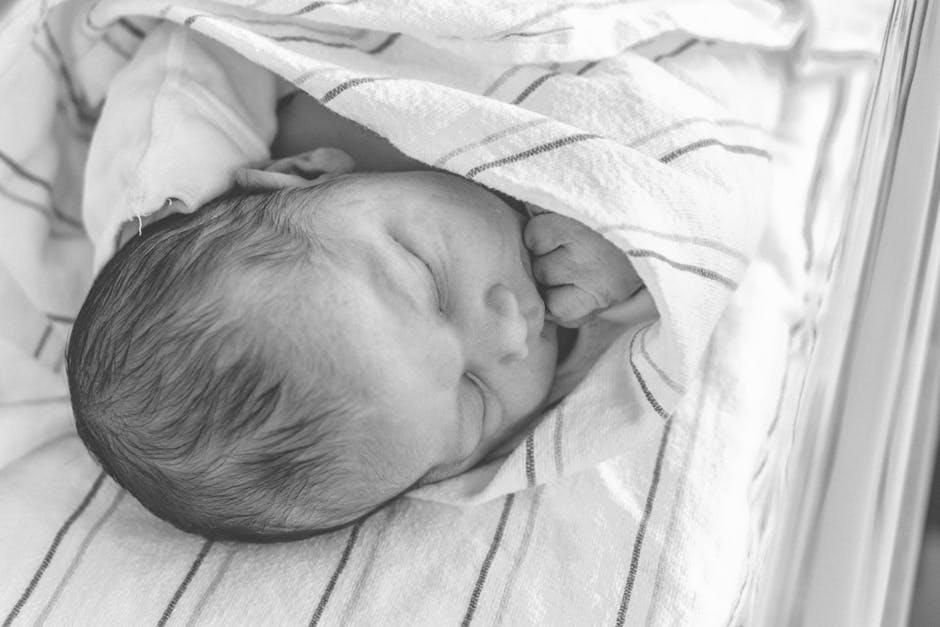 A serene black and white photo of a newborn baby sleeping peacefully, wrapped in a soft blanket.
