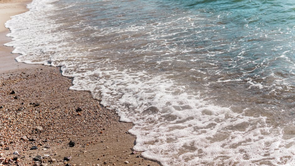 Peaceful beach scene featuring gentle waves rolling over small pebbles and sand.