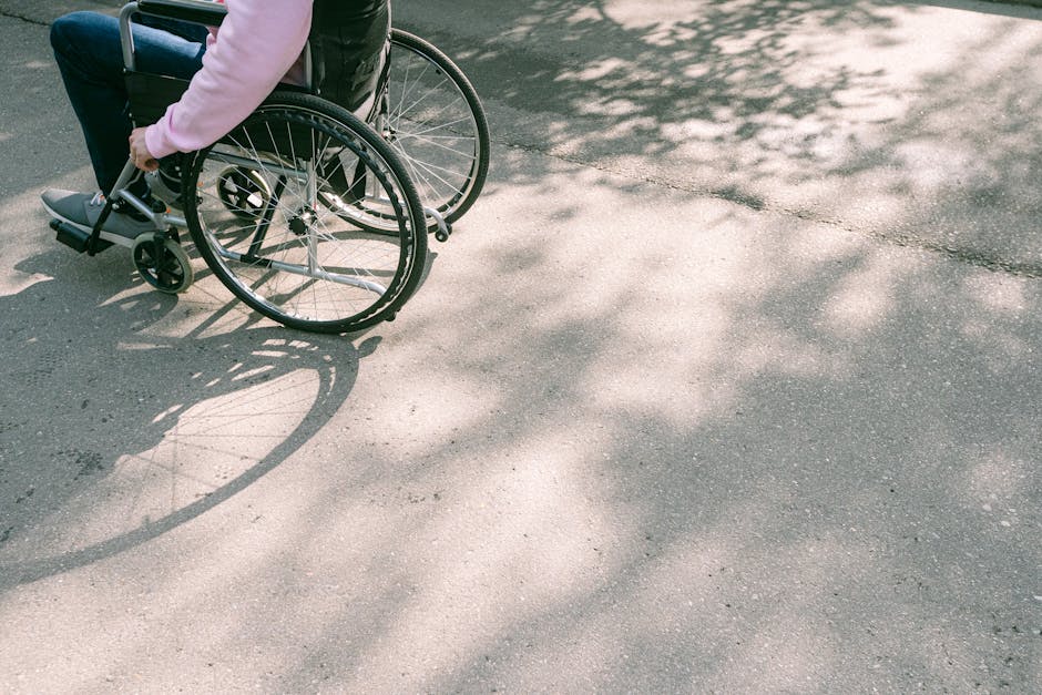 A person in a wheelchair navigating a sunlit road with tree shadows. The image captures a moment of mobility and independence.