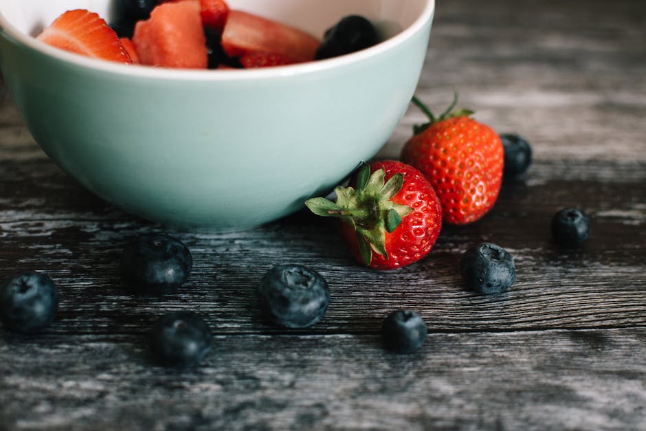 Close-up of fresh strawberries and blueberries in a ceramic bowl on a rustic wooden table.