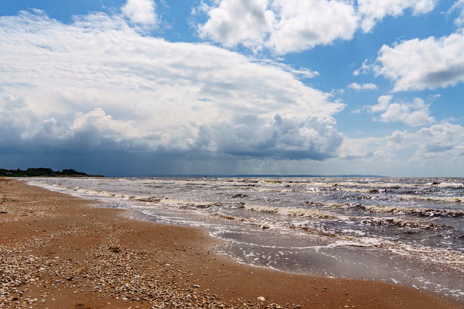 Wide sandy beach under dramatic clouds and blue sky, capturing a vibrant coastal scene.