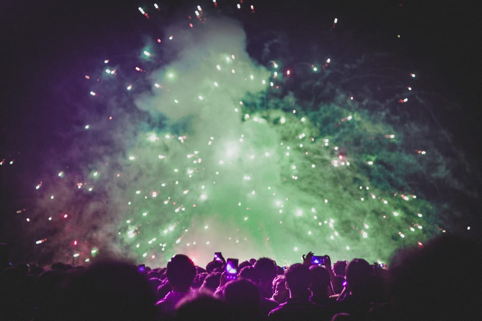Crowd watches a stunning fireworks display at night with colorful smoke and bright lights.