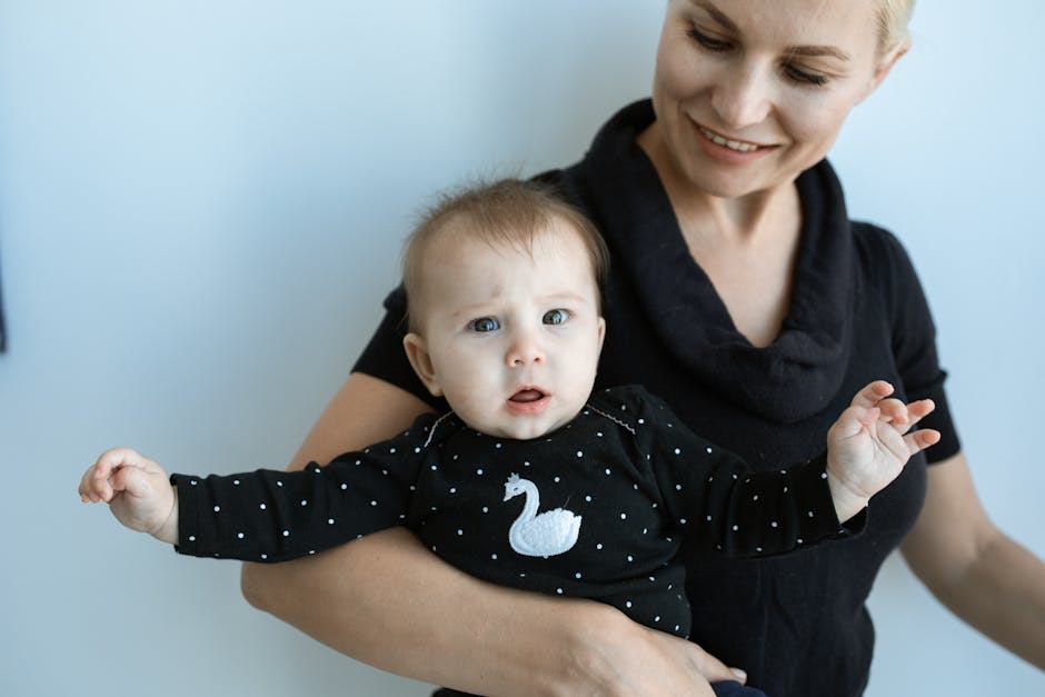 A mother holds her smiling baby in a black outfit with swan design indoors.