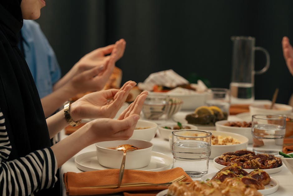 People gathered around a table praying before an iftar dinner during Ramadan, showcasing cultural and religious practices.