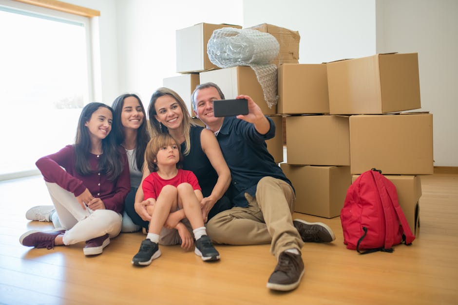 Family sitting together surrounded by boxes, capturing a selfie marking their new beginning.