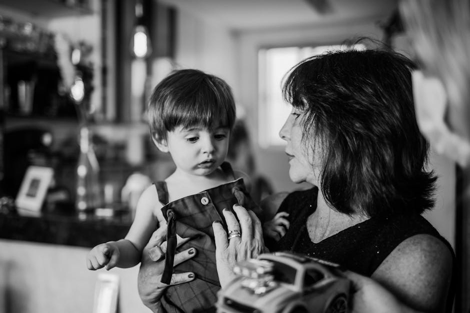 Black and white photo of a grandmother holding her toddler grandson, capturing a candid indoor moment.