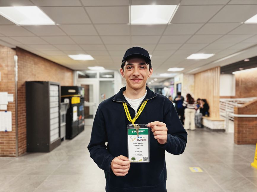 A young student smiling while holding an ID badge in a school hallway, conveying friendliness.