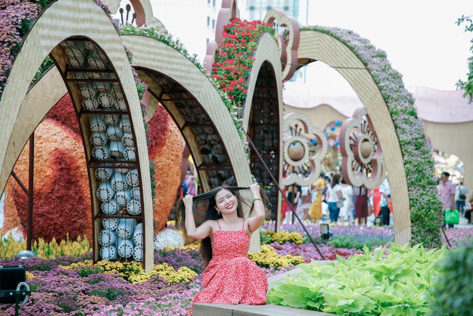 Smiling woman in red dress enjoying a vibrant floral garden display outdoors.
