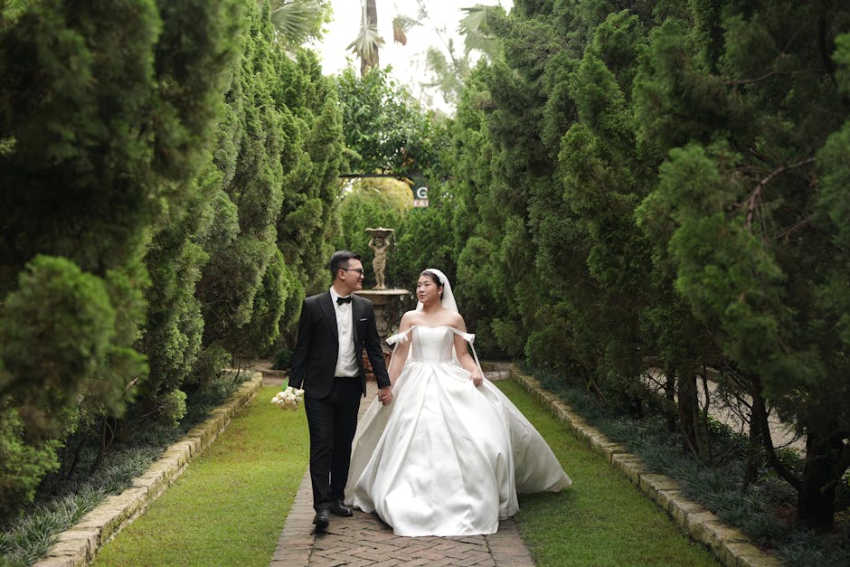 A bride and groom walk through a lush, green garden path, exuding elegance and joy on their wedding day.