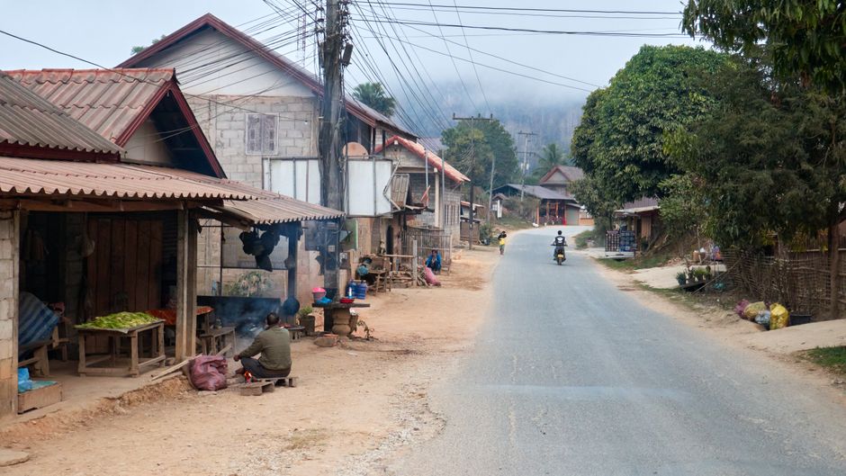 Rustic village street scene in Laos, capturing daily life with locals and traditional houses.